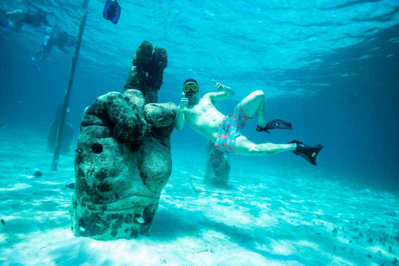 Snorkeling man doing the OK gesture beside an underwater sculpture of a big human hand